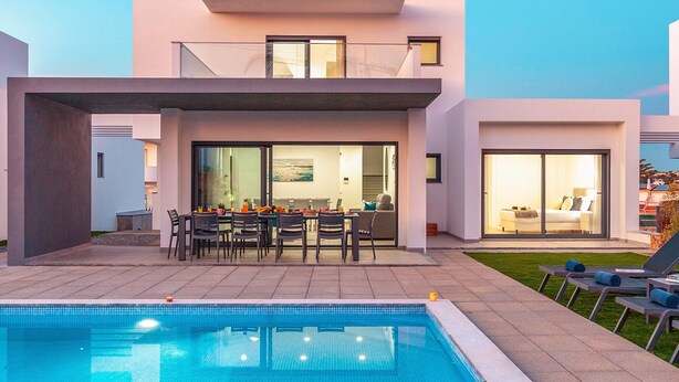 Ein modernes, zweistöckiges Haus mit Swimmingpool, Essbereich und einem Schlafzimmer, das durch große Glaswände sichtbar ist.