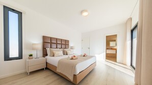 Ein modernes Schlafzimmer mit einem großen Bett, Nachttischen, einem Fenster und Blick auf ein Badezimmer.