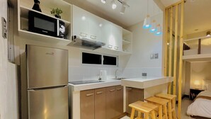 Une cuisine compacte équipée d’un réfrigérateur, d’un four à micro-ondes et d’une cuisinière. On y trouve des tabourets en bois et une petite table.