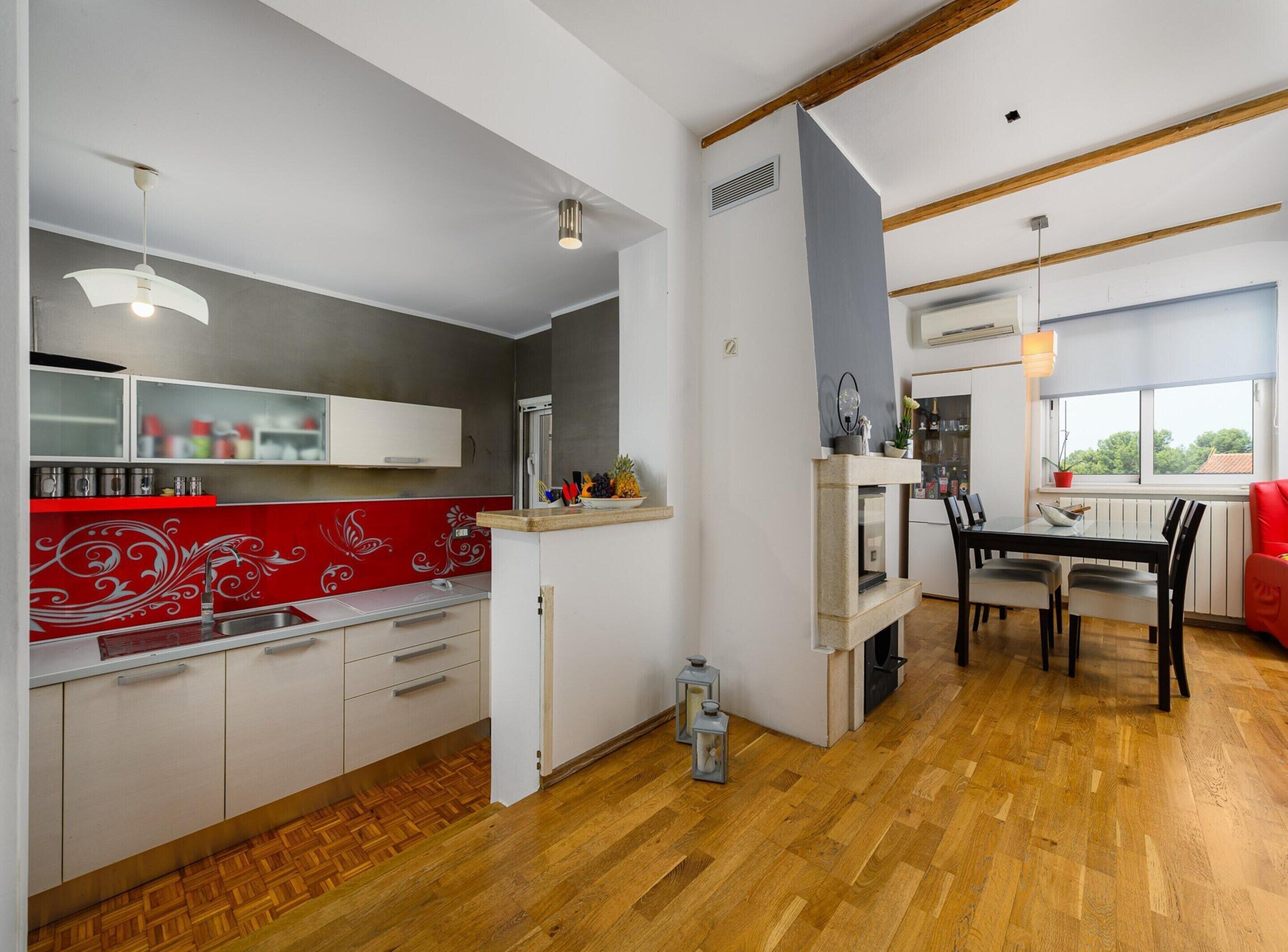 A modern kitchen with white cabinets, a red backsplash, and a dining area with a wooden table and chairs.