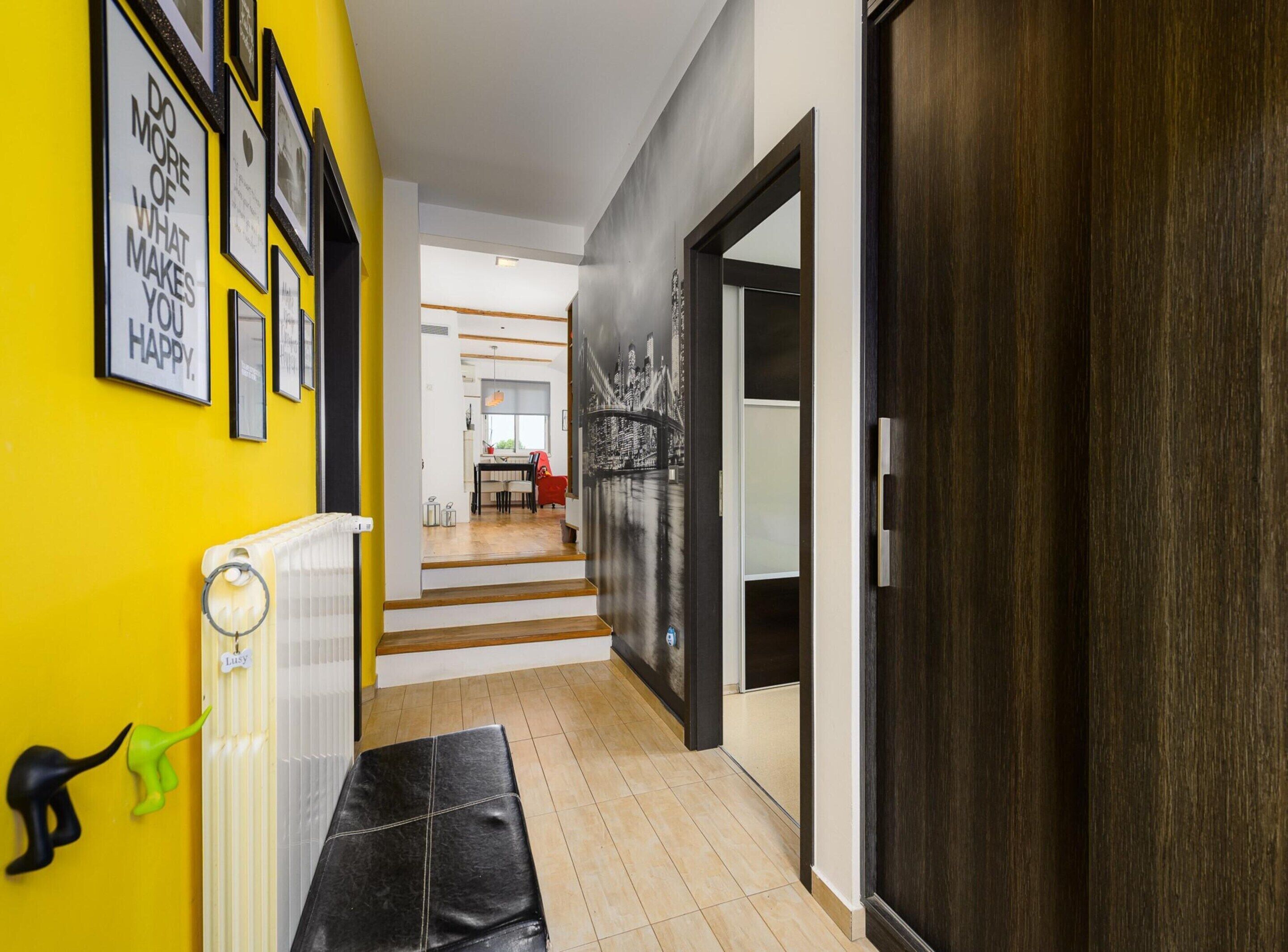 A hallway with a yellow wall, framed motivational quotes, a radiator, a black bench, and a staircase leading to a dining area.