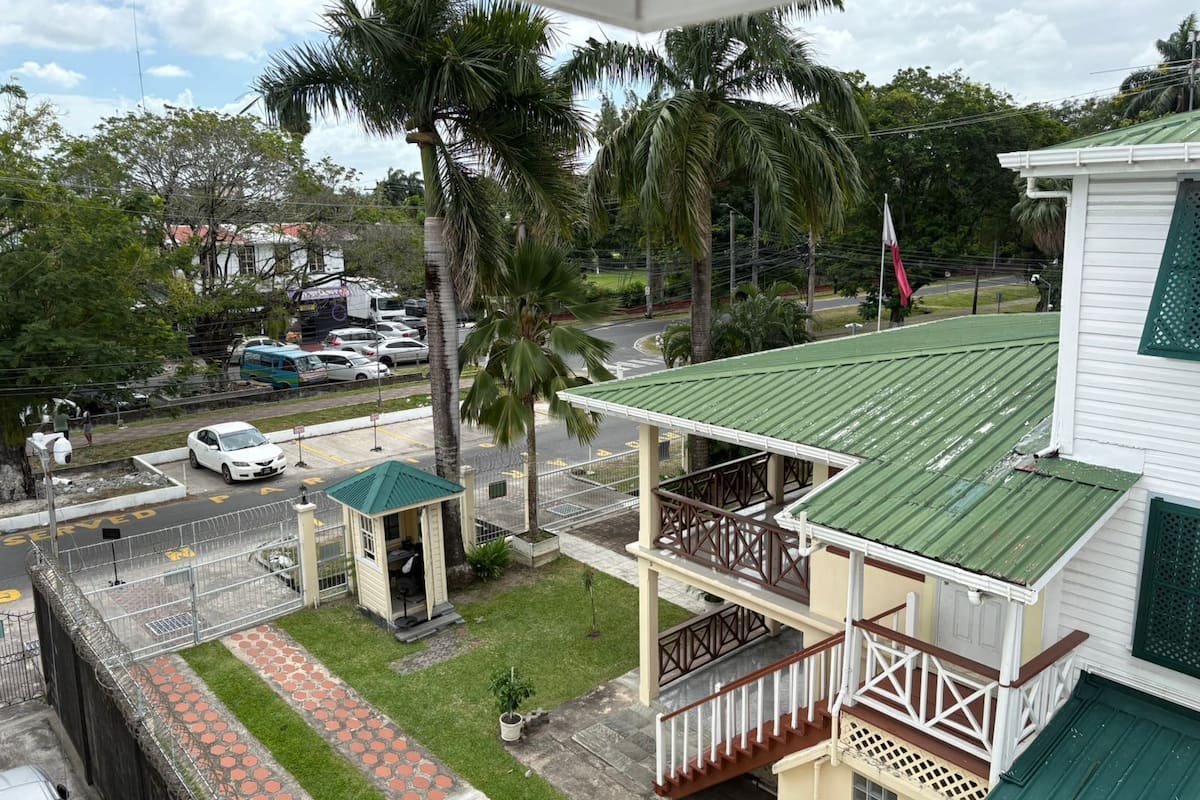 A two-story building with a green roof, a covered porch, and a small garden area.