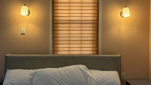Ein Hotelzimmer mit Bett, einem Fenster mit Jalousien und zwei Wandleuchten.