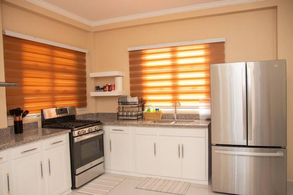 A modern kitchen with white cabinets, stainless steel appliances, and a window with blinds.