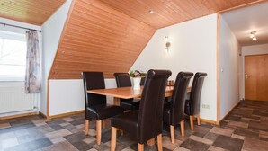 A dining area with a wooden table and chairs, a potted plant, and a sloped ceiling. - House Hafeneck FeWo Deichblick (Bensersiel)