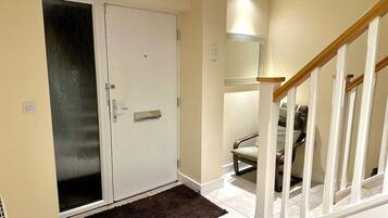 A hallway with a white door, a dark rug, a chair, and a staircase.