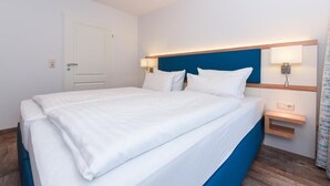 A hotel room with a bed, bedside lamps, a nightstand, and a door.