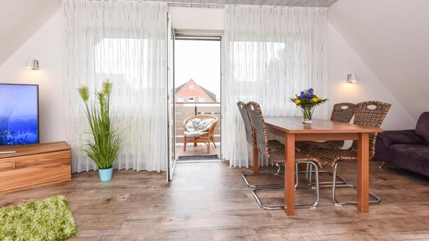 Ein Essbereich mit Holztisch und Korbstühlen, einem Fernseher auf einem Holzschrank und einer Topfpflanze.