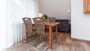 Ein Essbereich mit einem Holztisch, Korbstühlen, einem violetten Sofa und einem weißen Vorhang.
