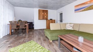 Ein modernes Wohnzimmer mit einem grünen Sofa, einem Holztisch und einer Essecke mit Korbstühlen.