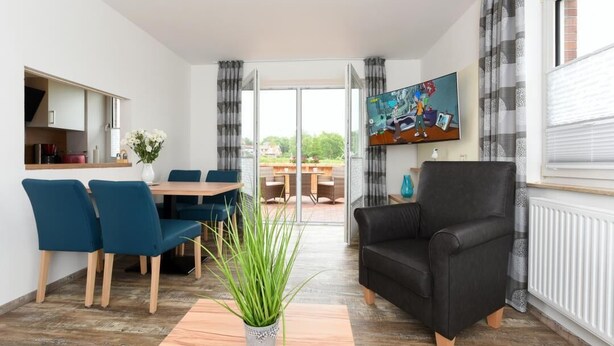 A modern living room with a dining area, a black leather sofa, and a TV mounted on the wall. - Haus zur Möwe apartment Möwe 1 (Bensersiel)