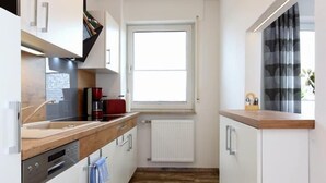 A narrow kitchen with white cabinets, a wooden countertop, and a window with curtains. - Haus zur Möwe apartment Möwe 1 (Bensersiel)