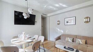 Uma sala de estar moderna com uma televisão de tela plana, um sofá e um espaço de jantar com cadeiras e uma mesa posta para quatro pessoas.