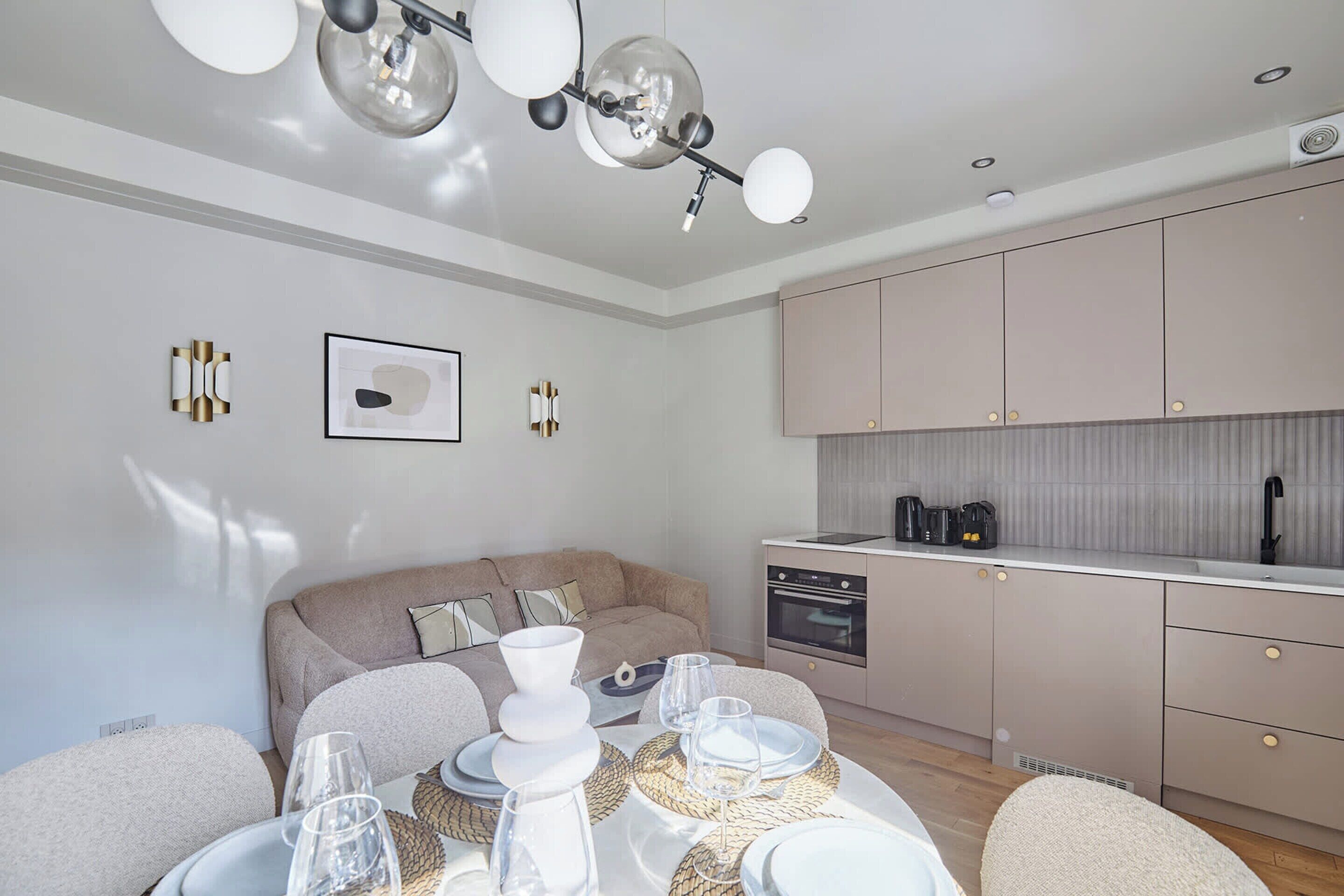 Una cocina moderna con electrodomésticos integrados, una zona de comedor con una mesa redonda y sillas, y un rincón de estar acogedor con un sofá.