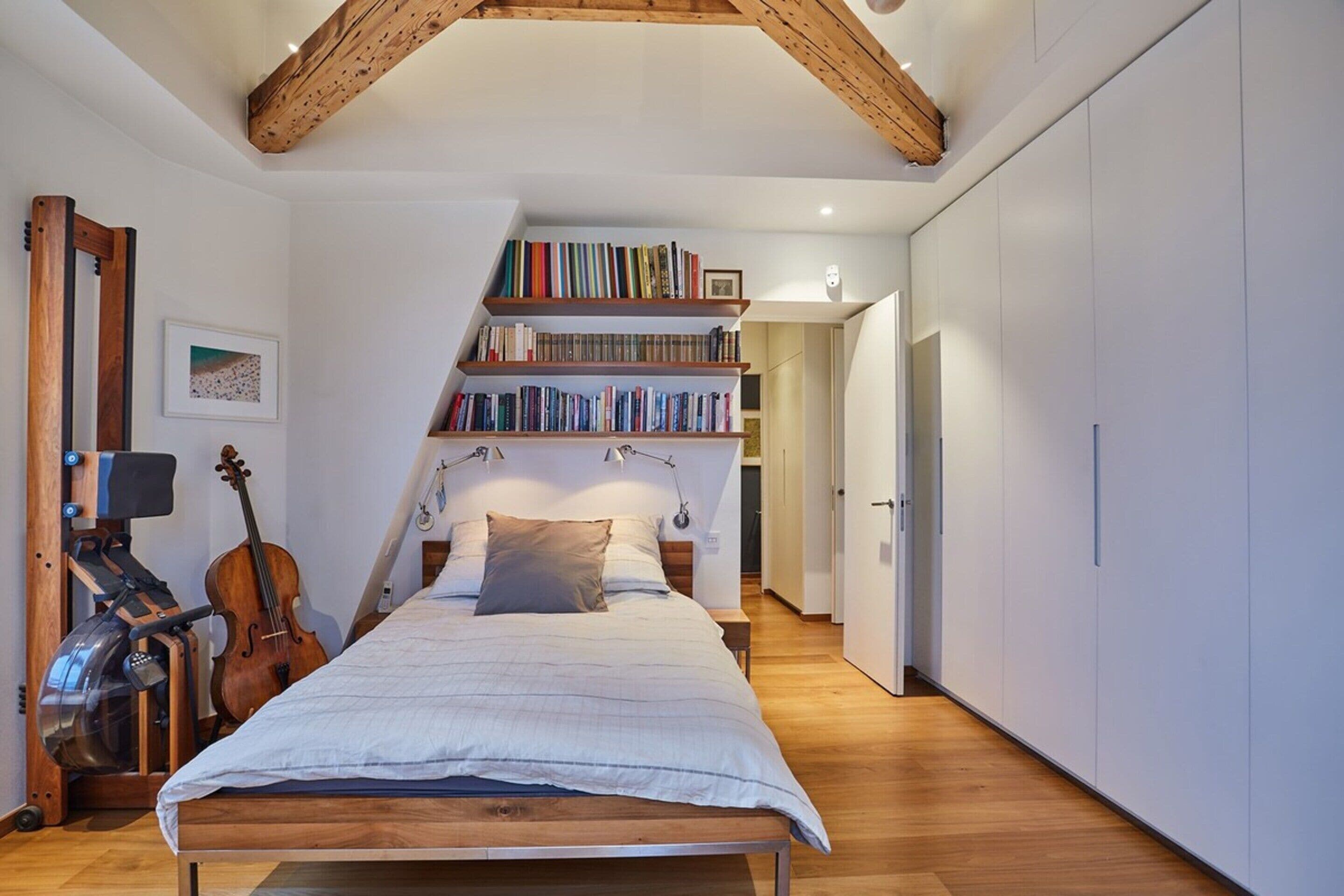Een slaapkamer met een houten bed, een viool, een boekenkast en een spiegel.