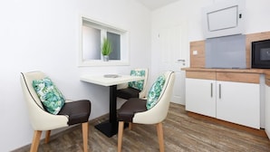 A small kitchen with a white countertop, a microwave, and a window with a plant. There are two chairs with leaf-pattern cushions and a small table. - Haus zur Möwe apartment Möwe 2 (Bensersiel)