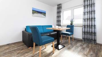 Una habitación con un sofá azul, dos sillas azules, una mesita de madera y una ventana con cortinas.