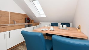 A modern kitchen with a skylight, white cabinets, and a wooden dining table with blue chairs. - Haus zur Möwe apartment Möwe 4 (Bensersiel)