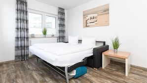 A modern bedroom with a large bed, a bedside table, a small desk, and a window with curtains. - Haus zur Möwe apartment Möwe 4 (Bensersiel)
