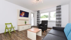 A modern living room with a sofa, a coffee table, a chair, and a TV mounted on the wall. - Haus zur Möwe apartment Möwe 5 (Bensersiel)