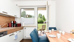 A modern kitchen with white cabinets, a wooden countertop, and a dining area with a table set for two. - Haus zur Möwe apartment Möwe 5 (Bensersiel)