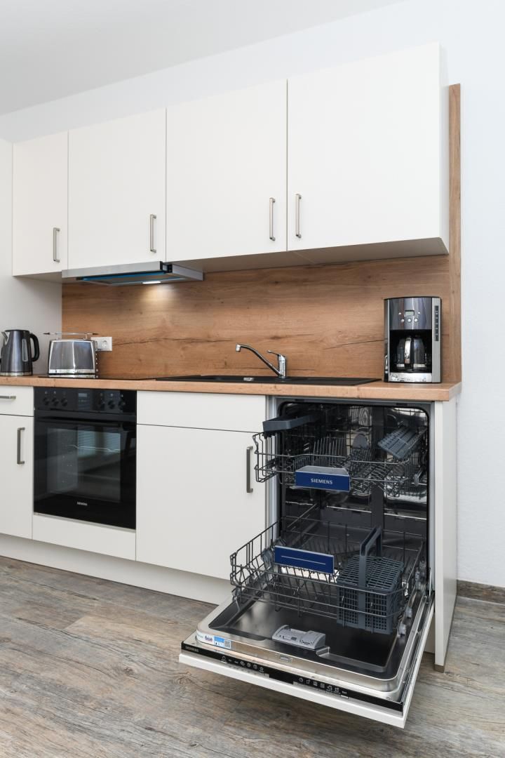 A modern kitchen with white cabinets, a wooden countertop, a built-in oven, a coffee maker, and a dishwasher.