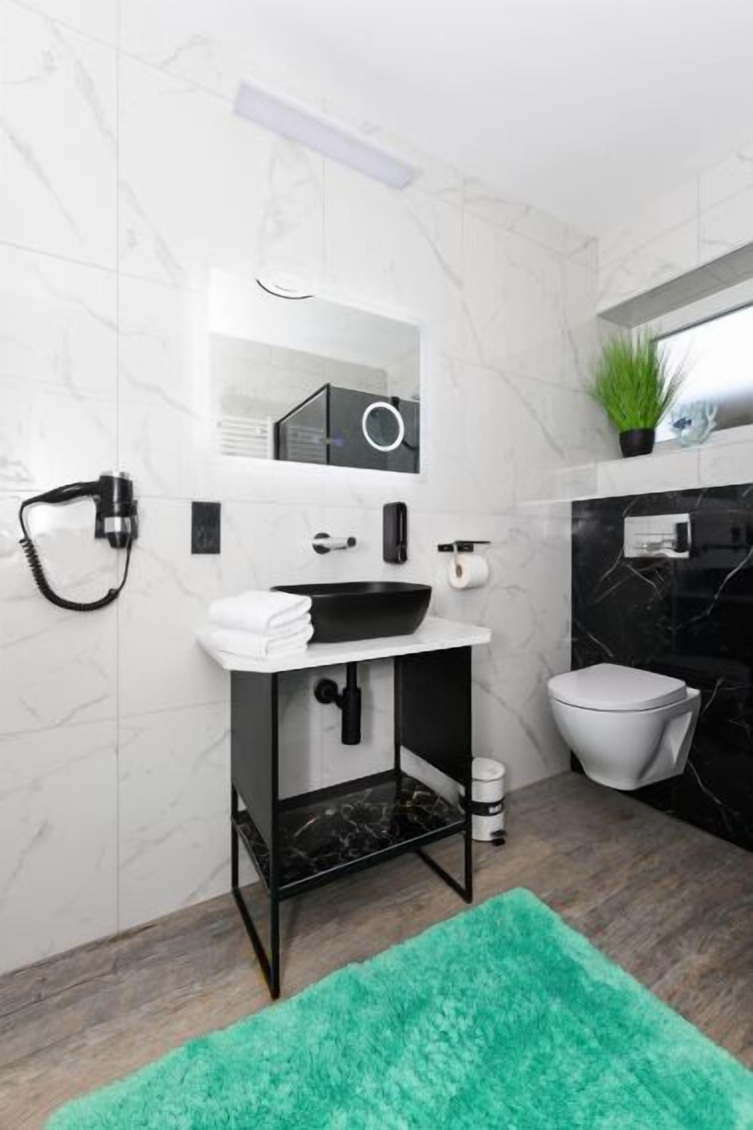 Ein modernes Badezimmer mit einem schwarzen Waschbecken, weißen Marmorwänden, einem grünen Teppich und einer Toilette.