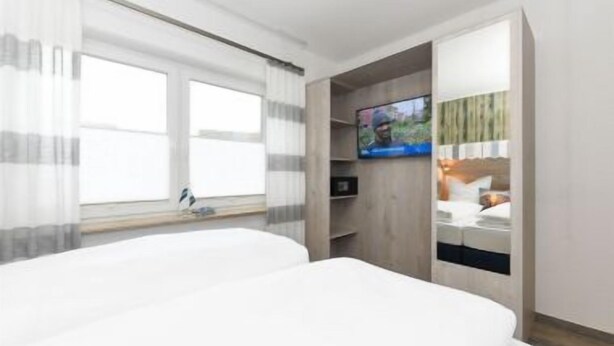 A hotel room with a large bed, a TV mounted on the wall, and a window with sheer curtains. - House Strandkorb apartment Strandkob 2 (Bensersiel)