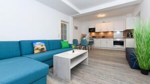 A modern living room with a blue sofa, a white coffee table, and a kitchen in the background. - House Strandkorb apartment Strandkob 2 (Bensersiel)