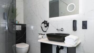 Ein modernes Badezimmer mit einer Duschkabine aus Glas, einer weißen Toilette, einem schwarzen Waschbecken mit Marmorplatte und einem Spiegel mit runder Beleuchtung.