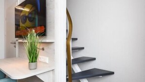 Una moderna scala con un design elegante, un televisore a schermo piatto montato su una parete bianca e una piccola pianta in vaso su un pianerottolo.