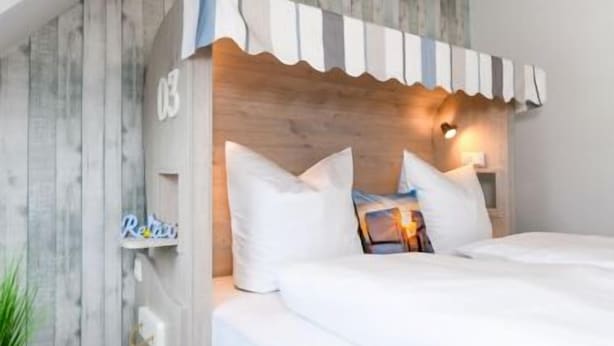 Una camera da letto con testiera in legno, biancheria da letto bianca e comodino con lampada.