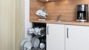 A compact kitchen with white cabinets, a wooden countertop, a coffee machine, and a dish drying rack. - House Strandkorb apartment Strandkob 6 (Bensersiel)
