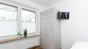 A bedroom with a large wardrobe, a television mounted on the wall, a window with blinds, and a radiator under the window. - House Strandkorb apartment Strandkob 6 (Bensersiel)