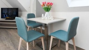 Ein moderner Essbereich mit einem weißen Tisch, türkisfarbenen Stühlen, einem Blumenstrauß und einem Fernseher im Hintergrund.