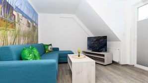 Ein modernes Wohnzimmer mit einem blauen Sofa, einem kleinen weißen Couchtisch und einem Flachbildfernseher auf einem weißen Schrank.