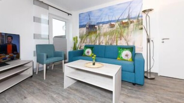 Un soggiorno moderno con un divano blu, un tavolino da caffè bianco e un quadro che raffigura una costa.