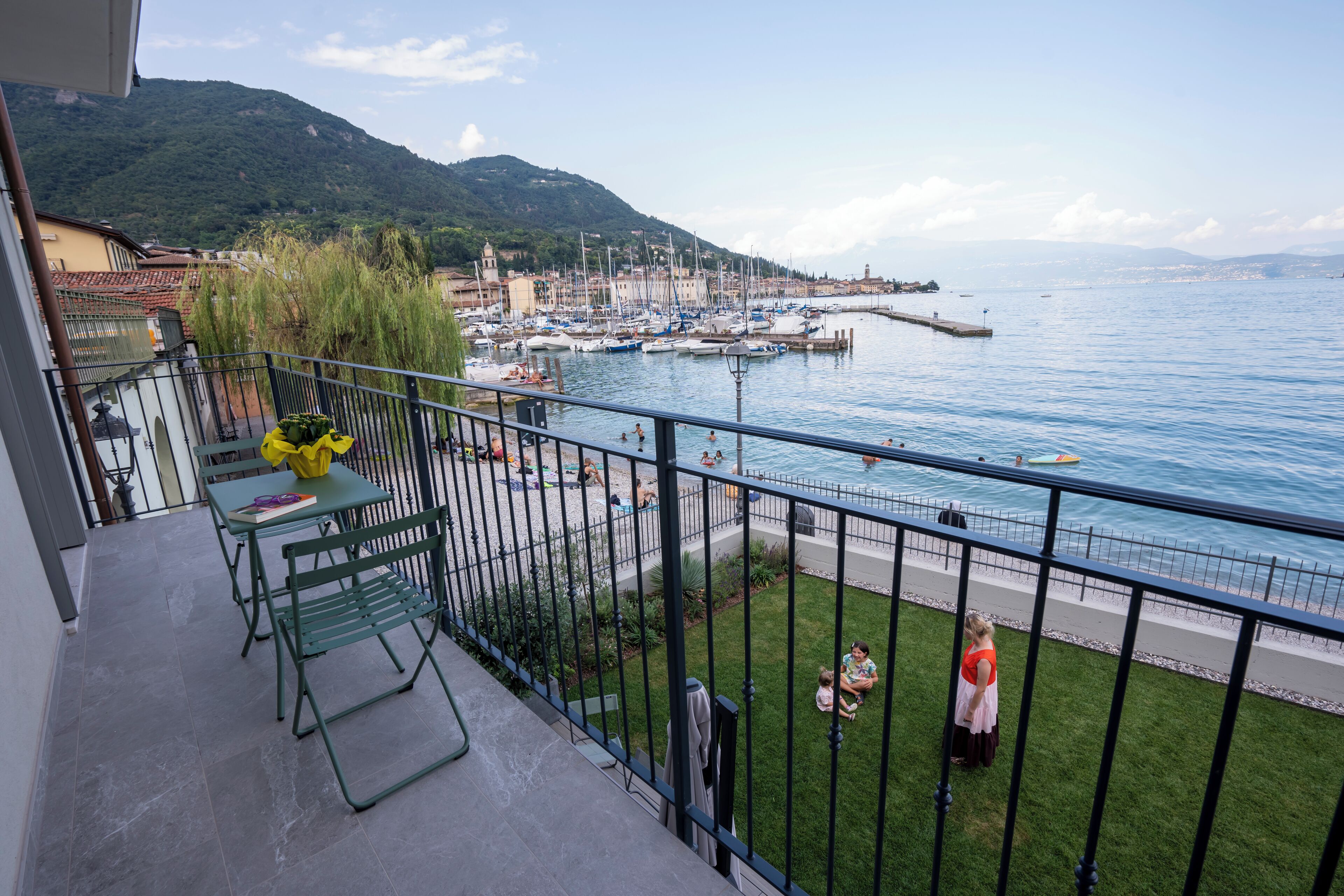 A balcony with a view of a marina, a grassy area, and a mountain in the background.