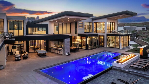 Une maison moderne dotée d’une piscine, d’un espace salon extérieur et de grandes fenêtres.