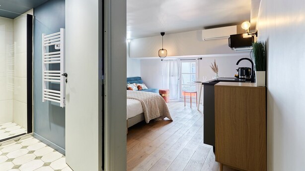 Een moderne slaapkamer met een bed, nachtkastje en uitzicht op de woonkamer.