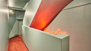 Een moderne hal met een rood tapijt, een neonbord waarop staat 'This is who' en een witte muur met een geometrisch ontwerp.