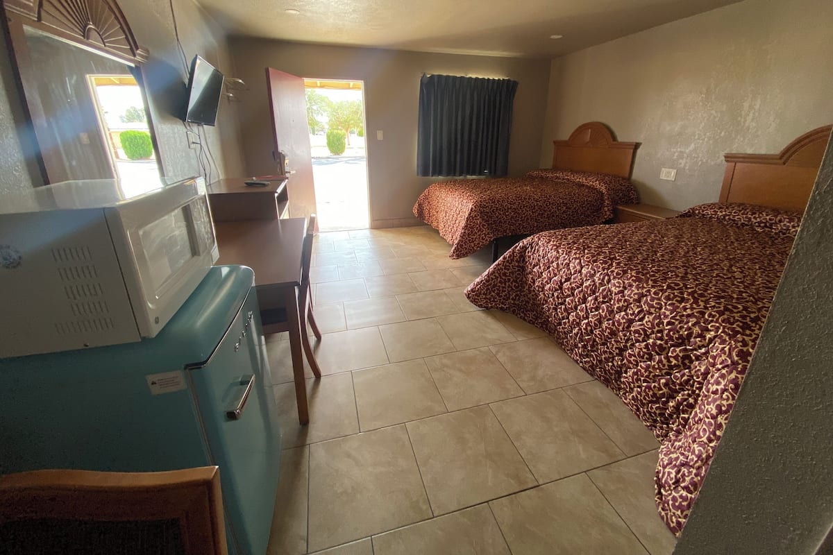 Una habitación de hotel compacta con dos camas, una kitchenette, un escritorio y un televisor.