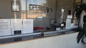 A reception desk with informational signs, a computer, and a plant. - Apple Valley Motel (Apple Valley)