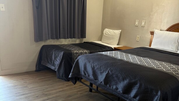 A hotel room with two beds, a wooden floor, a window with curtains, and a plain wall. - Apple Valley Motel (Apple Valley)
