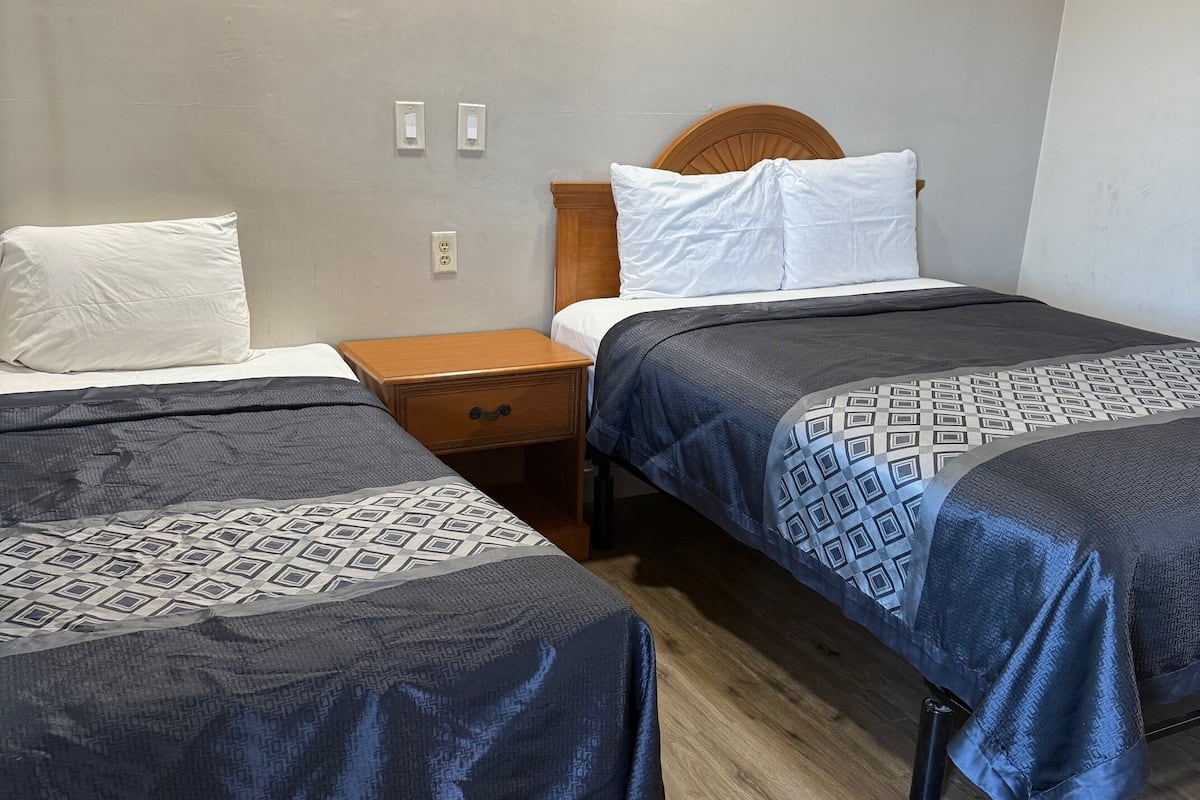 Una habitación con dos camas, cada una con ropa de cama estampada, una mesita de noche de madera y un cabecero de madera.