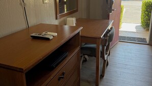 A hotel room with a wooden desk, a television mounted on the wall, a mirror, and a door leading to a parking area. - Apple Valley Motel (Apple Valley)