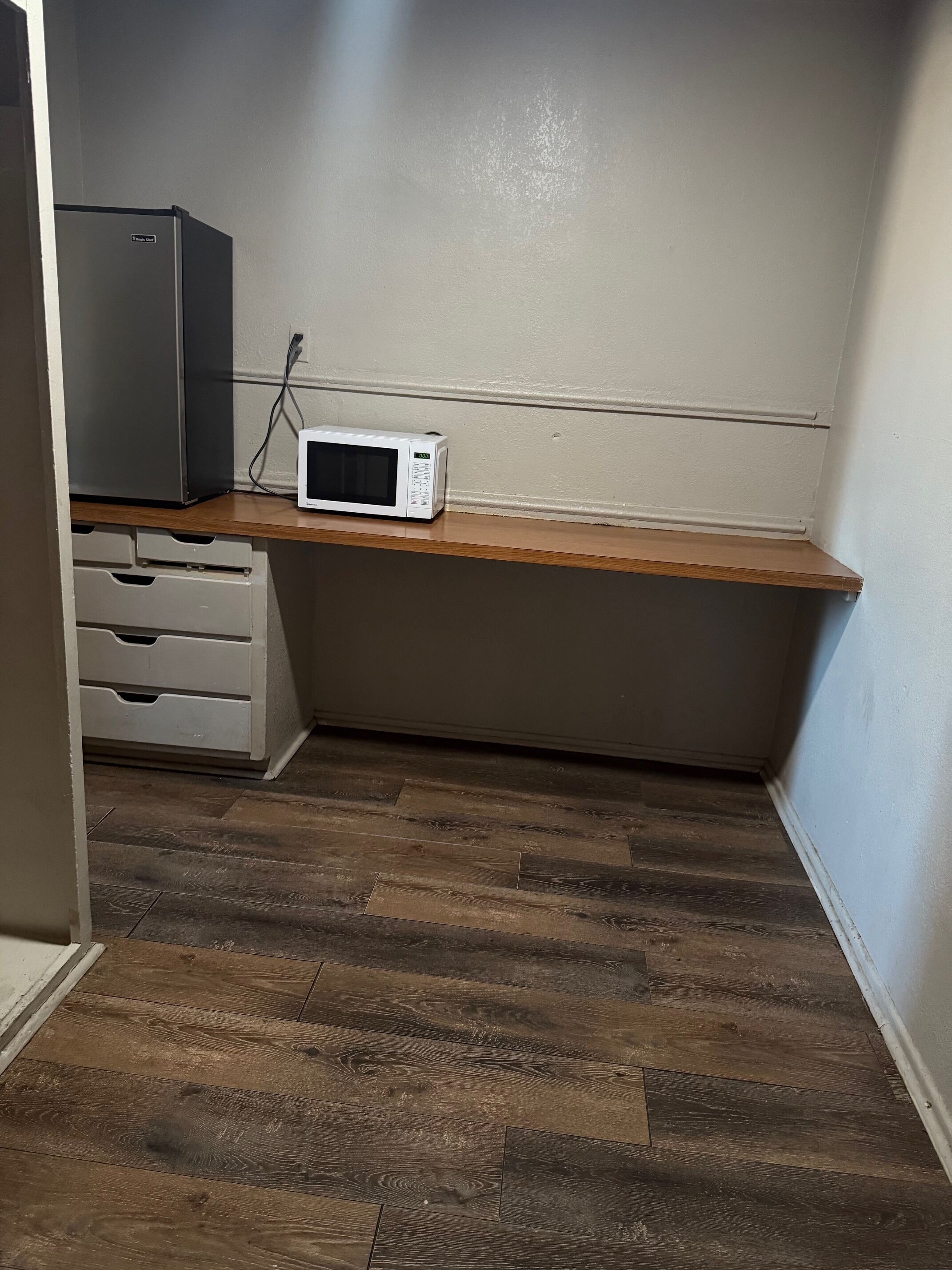 Una pequeña kitchenette con microondas, refrigerador y encimera de madera.