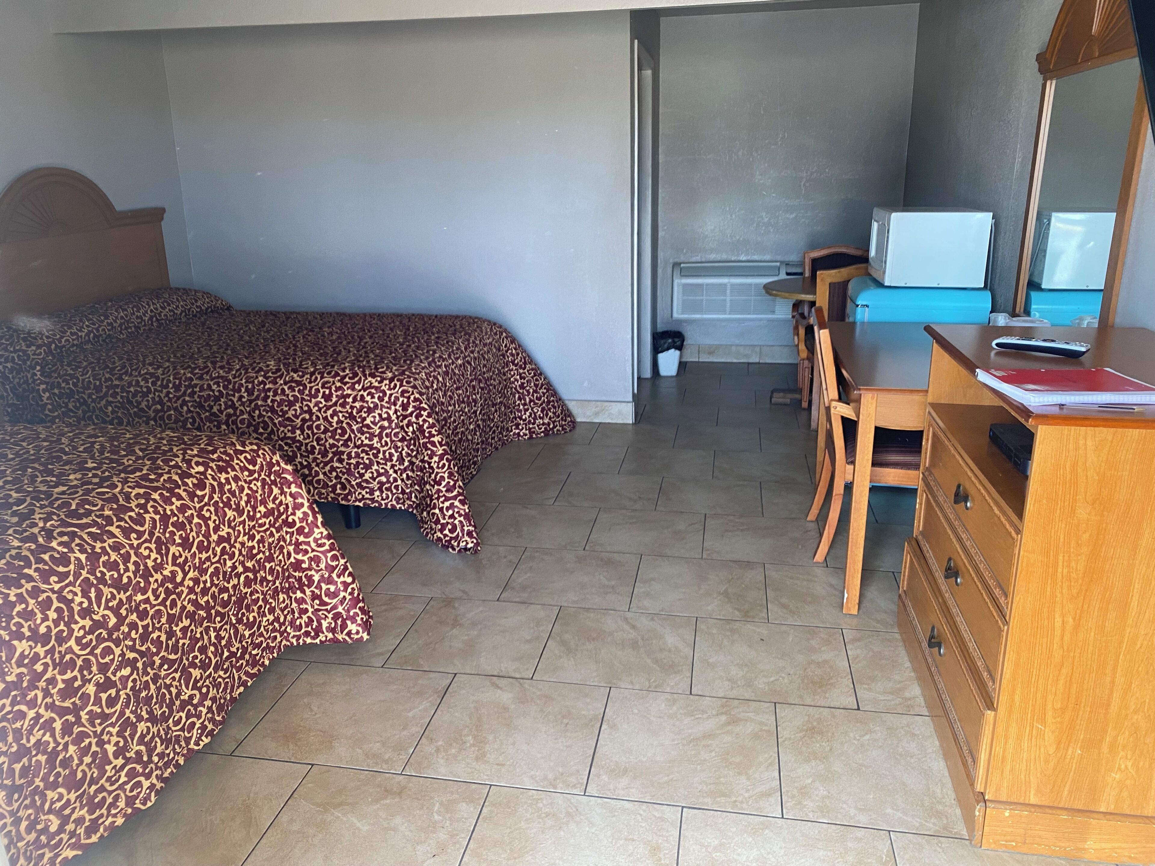 Ein Hotelzimmer mit zwei Betten, einem Schreibtisch, einem Stuhl, einer Kommode und einer Mikrowelle.