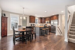 Une cuisine moderne avec des meubles de couleur bois foncé, un îlot central doté de tabourets, un réfrigérateur en acier inoxydable et un escalier menant à un niveau supérieur.