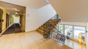 A modern hotel interior with a staircase, a hallway leading to the reception, and a view of the outdoors through large windows. - Hotel Franken (Forchheim)